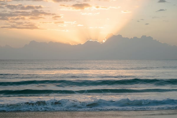 Sunrise bursting through clouds over turquoise surf and white sand beach at dawn